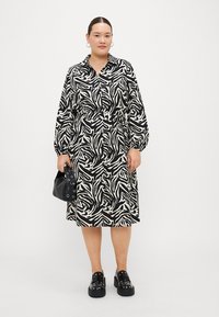 Black and white zebra print shirt dress with a collar, cinched waist, and long sleeves, paired with black bag and chunky shoes.