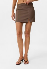 Bruine mini-jurk met een rechte zoom, voorzien van een zijsplits voor extra detail. Gemaakt van een gladde stof, heeft het een getailleerde silhouet.