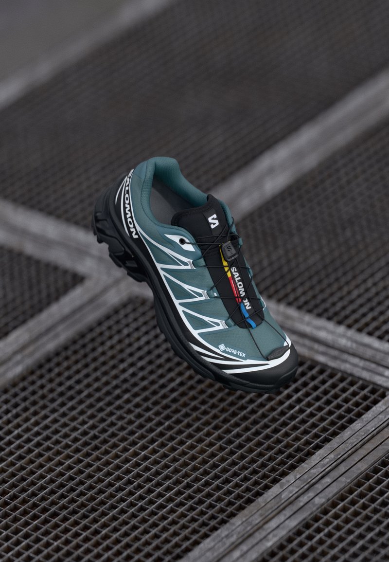 Teal and black running shoe featuring a GORE-TEX label, streamlined design, white accents, and a quick-lace system on a textured surface.