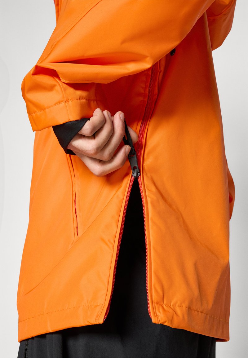 Giacca impermeabile di un brillante arancione, dotata di una ventilazione laterale con zip, polsini elastici e un taglio moderno. Il materiale appare liscio e leggero.