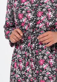 Blumenkleid mit schwarzem Hintergrund, das mit rosa, weißen und grauen Blumen verziert ist; tailliert mit einer zum Binden versehenen Detail; lange Ärmel.