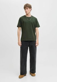 Camiseta de algodón verde oscuro con cuello redondo, combinada con pantalones vaqueros negros holgados. Accesorios con un collar de cadena de plata.