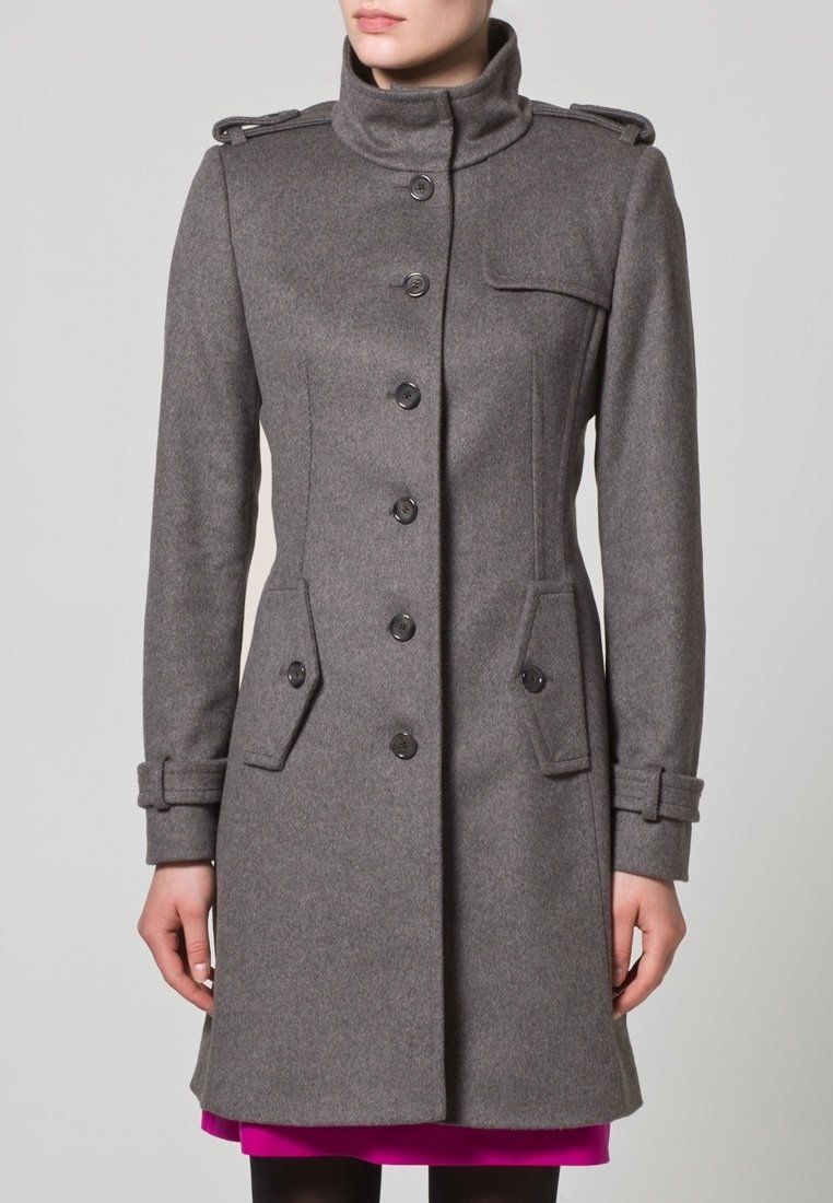 Harmaa villakangastakki, jossa korkea kaulus, napitettava suljenta, sivutaskut ja olkatoppaukset; takissa on istuva leikkaus ja teksturoitu kangas.