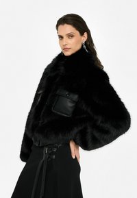 Giacca in ecopelliccia nera con colletto alto, vestibilità oversize e dettagli in pelle. Presenta tasche frontali e polsini a coste.