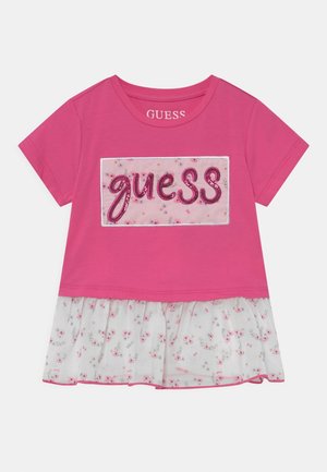 Robe rose à manches courtes avec le mot « guess » en sequins roses sur un panneau floral pâle et un ourlet à volants à fleurs blanches.