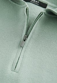 Hele roheline neljandiku tõmblukuga pullover, mis on valmistatud tekstuuriga kangast. Omab metallist tõmblukku ja ümarat kraed. Silt ütleb "NEXT."