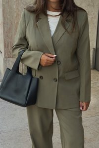 Oliwkowy, dopasowany garnitur z podwójnym guzikiem oraz dopasowanymi spodniami, w połączeniu z usztywnioną czarną skórzaną torebką.