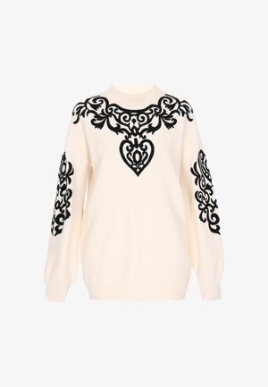 Kermävänvärinen neule, jossa on mustia brodeerattuja koristekuvioita rinnassa ja hihoissa. Ominaisuuksiin kuuluu pyöreä kaula-aukko ja resorit.