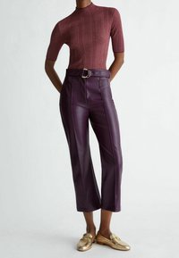 Viininpunainen ribbineuloksinen lyhythihainen paita yhdistettynä korkeavyötäröisiin, tummanpurppuranvärisiin tekonahkahousuihin, joissa on kullanvärinen solkivyö ja suorat lahkeet.