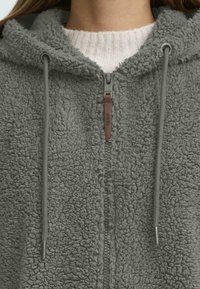 Grauer Fleece-Hoodie mit strukturierter Oberfläche, ausgestattet mit einem Reißverschluss vorne und einer Kapuze mit Zugband. Akzentuiert mit braunen Lederdetails am Reißverschluss-Zipper.