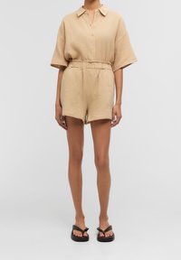 Ensemble en tissu texturé comprenant une chemise beige à col et un short, avec un devant à boutons, une taille élastique et une coupe décontractée, associé à des tongs.