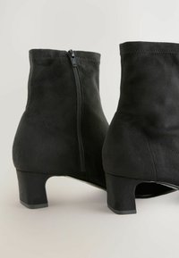 Bottines en daim noir avec une fermeture éclair sur le côté, un talon block effilé et des coutures sans couture pour une texture lisse et une silhouette structurée.