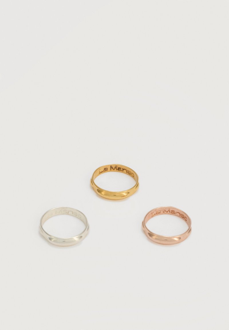 Tres anillos lisos de metal en plata, oro y oro rosa, cada uno grabado con "La Manso" en el interior.