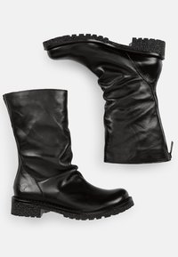 Botas de tobillo de cuero negro con una textura suave y arrugada, suela de goma negra gruesa y detalle de cremallera lateral para un fácil uso.