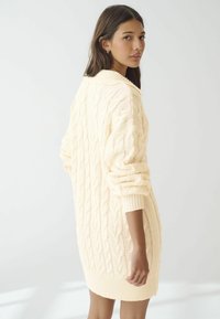 Robe pull en tricot avec câbles, d'un doux coloris crème, dotée d'un col et de poignets côtelés, de manches longues et d'une silhouette décontractée. Motif texturé sur l'ensemble.