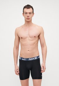 Črne bokserice iz elastičnega materiala z modrim in belim Nike logotipom na pasu. Oblikovane za udobje in tesno prileganje.