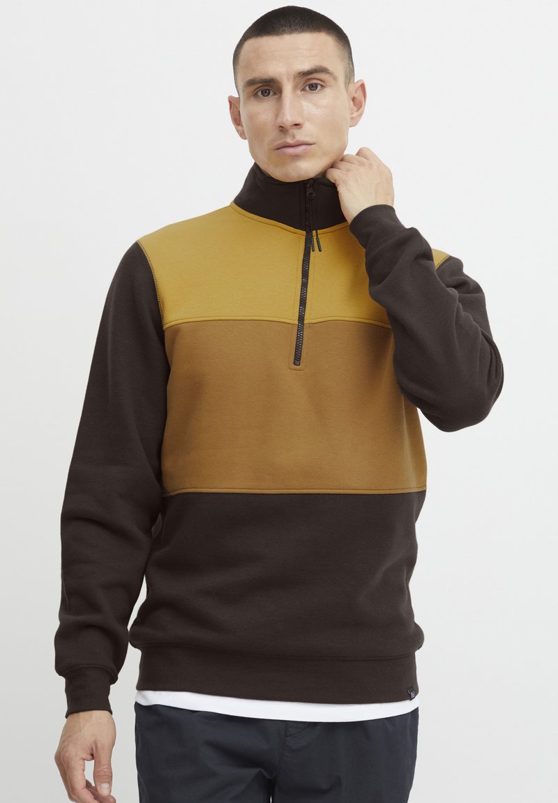 Fleece-Pullover in Braun und Senfgelb, mit einem Reißverschlusskragen, langen Ärmeln und einem Farbblockdesign mit glatter Textur.