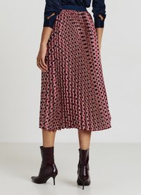 Jupe plissée rouge avec un motif géométrique circulaire. Portée avec un haut bleu marine ajusté et des bottines noires brillantes.