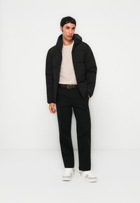 Black puffer jacket with a hood, featuring quilted design. Paired with a cream sweater and black trousers, complemented by white sneakers.