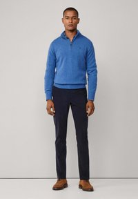 Suéter de punto azul claro con cuello con cremallera, combinado con pantalones azul marino oscuros y zapatillas de ante marrón. Diseño sencillo, textura suave. Logo de acento visible.