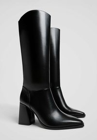 Bottes noires en cuir, montant jusqu'au genou, avec un bout pointu et un large talon block. Texture lisse avec un design simple et épuré.