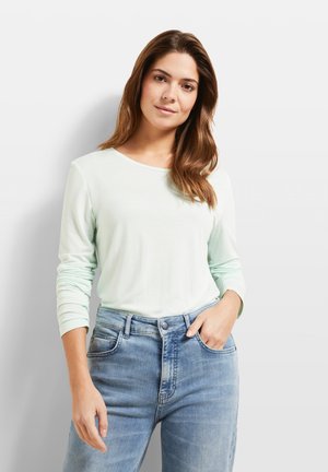 Hellgrünes langärmliges T-Shirt mit Rundhalsausschnitt, kombiniert mit hellblauen hoch taillierten Jeans, die sanfte Verblassungen und Taschen aufweisen.