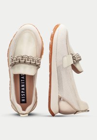 Zapatos de lona color beige sin cordones con detalles trenzados, fabricados en malla y cuero sintético. Presentan una suela de goma naranja texturizada para un mejor agarre.