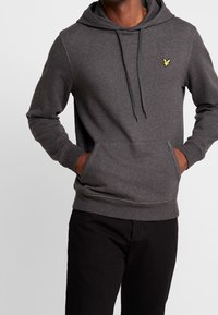 Szara bluza z kapturem wykonana z miękkiego materiału, z przednią kieszenią, ściągaczem w kapturze i małym żółtym logo na lewej piersi.