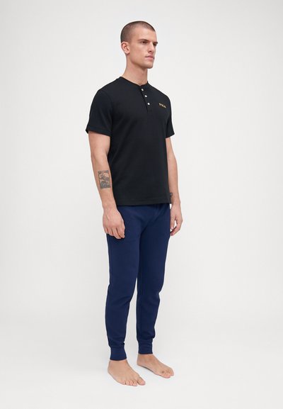 Polo preto de manga curta com tecido texturizado e placket de três botões, combinado com calças de fato slim-fit azul-marinho.