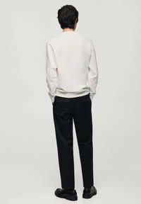 Witte sweatshirt met een ronde hals, gecombineerd met zwarte broeken. De outfit heeft een relaxte pasvorm en een zachte textuur, aangevuld met zwarte schoenen.