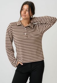 Polo majica s dugim rukavima prugasta u bež boji s tamnosmešnim prugama, s kragnom i plaketom s tri dugmeta, izrađena od mekog materijala.