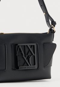 Black Armani Exchange shoulder bag with wide belt detail and large shiny black logo plaque, gold zipper, and adjustable strap.