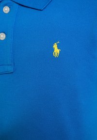 Camisa polo azul de algodón texturizado con una abertura de tres botones y un logo bordado en amarillo de un caballo y un jinete en el pecho.
