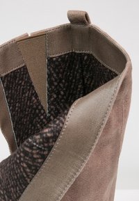 Hnědé semišové kotníkové boty s elastickým bočním panelem a tmavě vzorovanou textilní podšívkou, ukazující textury vnitřního a vnějšího materiálu.