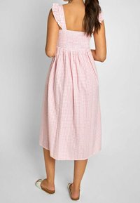 Rosa rutigt midiklänning med volangärmar och smockad byst, med en flödande kjol som når under knäet. Bärs med platta sandaler.