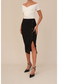 Vit off-shoulder topp med en omslagdesign, ihopparad med en svart pennkjol med en sidoklyvning och sex knappdetaljer. Svarta högklackade skor.