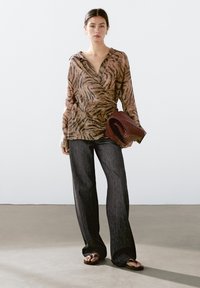Let ærme, langærmet indpakningsbluse med tigerstribe-mønster i beige og sort; parret med mørke, vide jeans og flade sandaler.