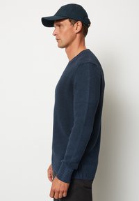 Marineblauer Strickpullover mit strukturiertem Finish, langen Ärmeln und geripptem Saum. Kombiniert mit einer passenden dunklen Mütze. Einfaches Design.