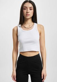 Bílý žebrovaný crop top bez rukávů s kulatým výstřihem a širokými ramínky, v kombinaci s černými legínami s vysokým pasem. Jednoduchý a přiléhavý design.