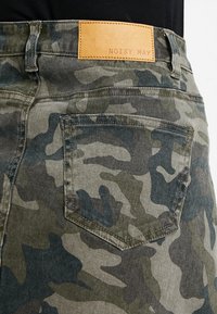 Kamoflage-mönstrade denimjeans bakficka med sömmar och en tanläder märkesetikett som säger "NOISY MAY" ovanför midjan.