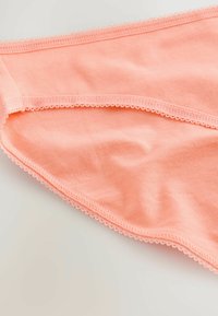 Perzikkleurige katoenen slipjes met een gladde textuur, voorzien van een delicate gegolfde rand langs de tailleband en beenopeningen.