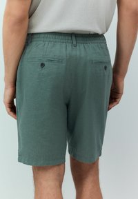 Pantaloni scurți din in verde cu talie elastică. Au două buzunare la spate cu închidere prin nasture, croi dreaptă și margini tivite.