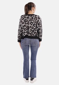 Maglione con stampa leopardata in grigio e nero, con orlo a coste, abbinato a jeans svasati blu e sneakers bianche con dettagli neri.