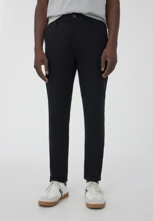 Pantaloni neri su misura realizzati in un tessuto morbido con una vestibilità slim. Presentano una chiusura con bottone anteriore e tasche sui lati.