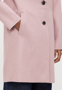 Ρόζ παλτό από μείγμα μαλλιού με ευθύγραμμο σχεδιασμό, με γιακά με έντονα σκισίματα, τρία μαύρα κουμπιά και πλαϊνές τσέπες. Μαλακή υφή με ελάχιστο φινίρισμα.