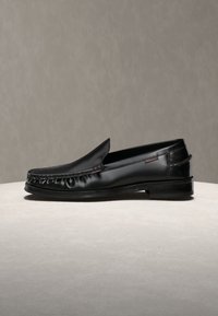 Mocassin noir en cuir avec bout mocassin cousu et petit talon, présenté de profil sur une surface plane avec un fond uni.