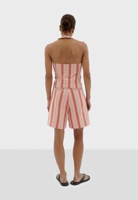 Tweedelige outfit met verticale roze en witte strepen. De top heeft een aansluitend strapless ontwerp; de shorts zijn los en hebben zijzakken.