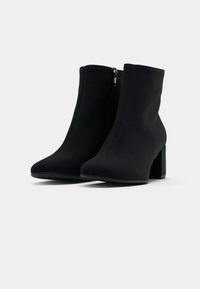Botas de tornozelo pretas com um acabamento liso e mate. Apresentam um bico afilado, um salto bloco médio e um fecho lateral para fácil colocação.