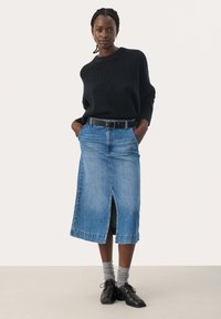 Schwarzer, weit gestrickter Pullover kombiniert mit einem blauen Jeans-Midirock mit einem Schlitz vorne. Gestylt mit einem schwarzen Gürtel, grauen Socken und schwarzen Schuhen.