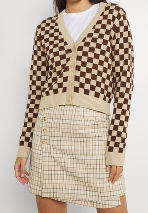 Cardigan à carreaux marron et beige avec un ourlet côtelé et cinq boutons, accompagné d'une mini-jupe en plaid beige avec des boutons sur les côtés.